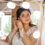Bride adjusting earrings while looking at her reflection in a mirror before wedding.