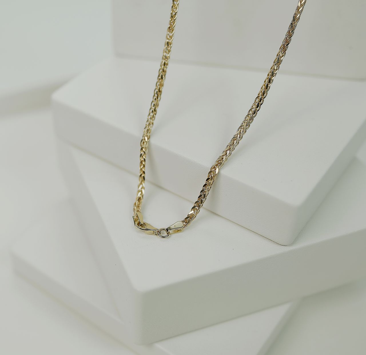 Close-up of a luxurious gold necklace elegantly displayed on a minimalist white platform.