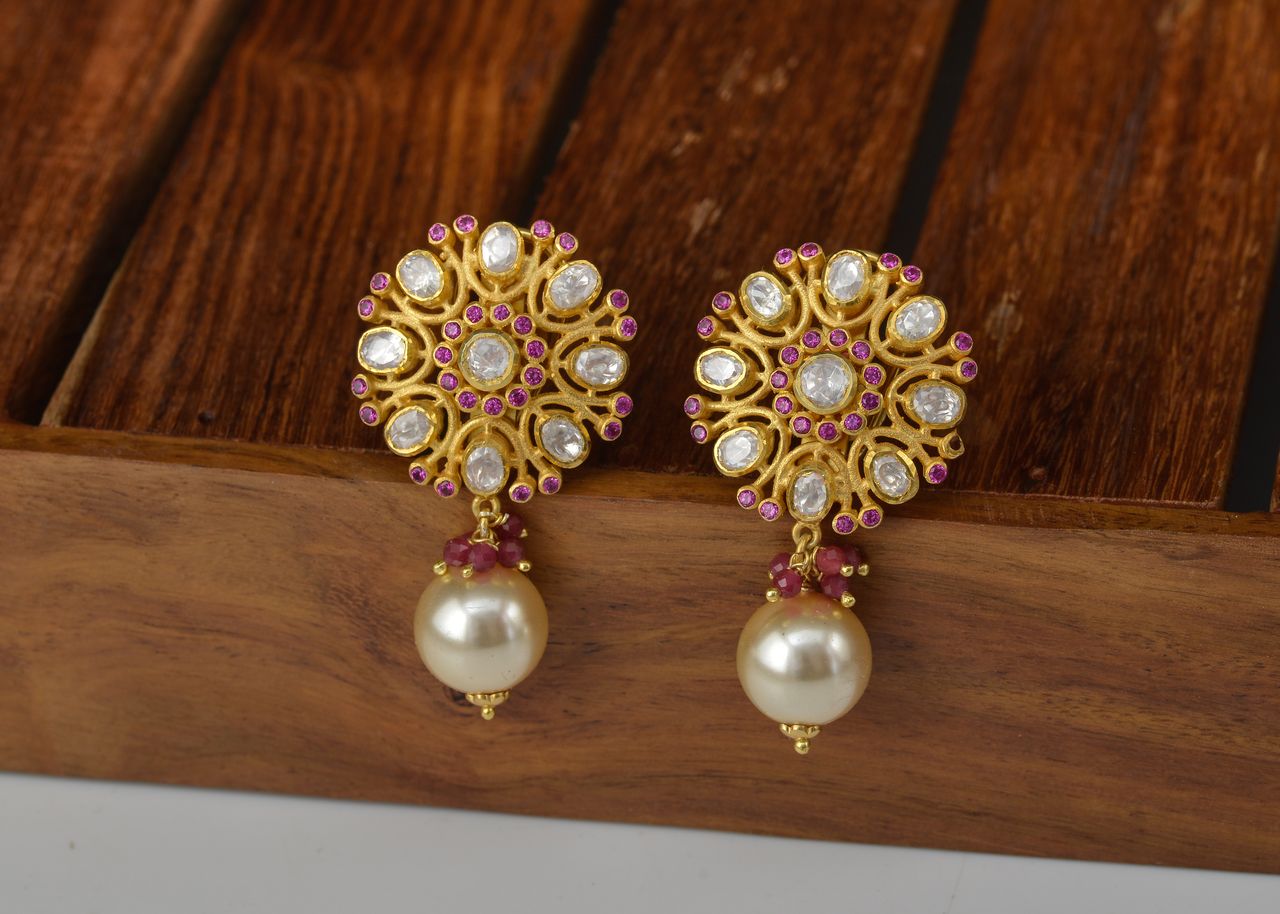 A sophisticated pair of gold earrings adorned with pearls and gemstones on wooden background.