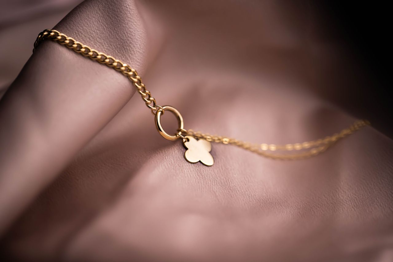 Close-up of a gold chain necklace with a clover pendant on a soft background, featuring elegant craftsmanship.