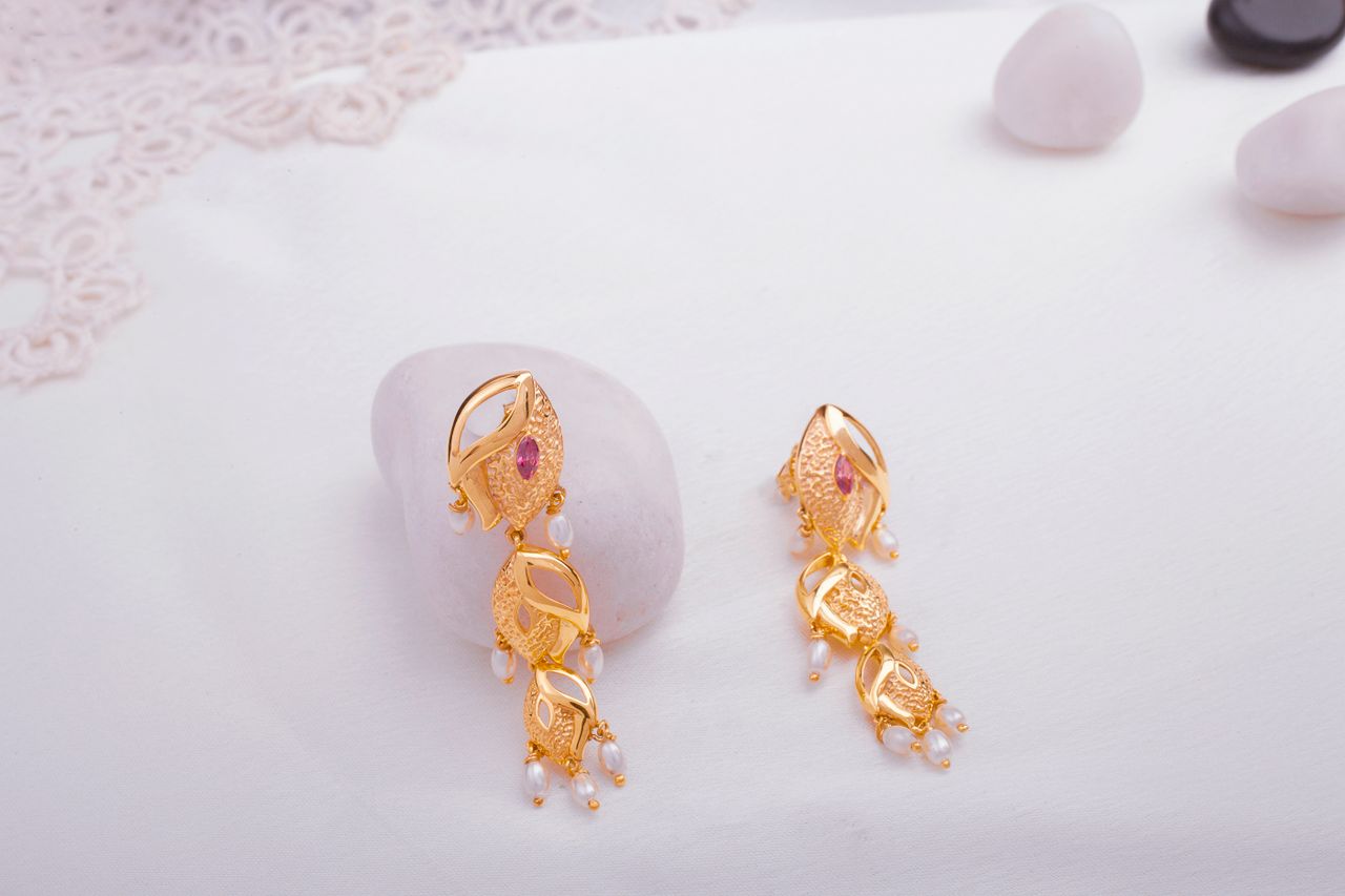 Gold earrings with gemstones and pearls displayed on a white marble surface.