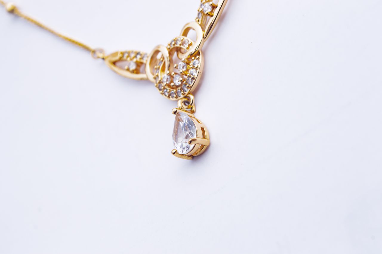 Close-up of a luxurious gold necklace with a diamond pendant on a white background.