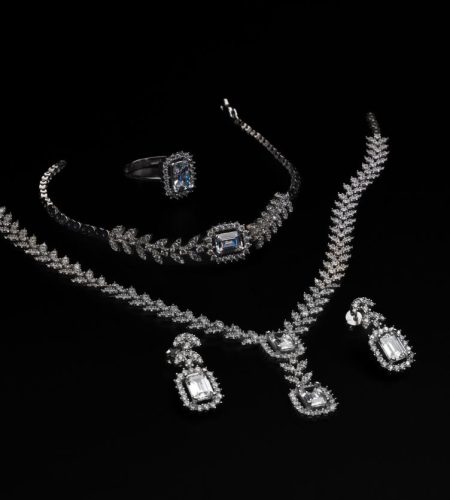 Elegant diamond jewelry set including necklace, bracelet, ring, and earrings on a black backdrop.